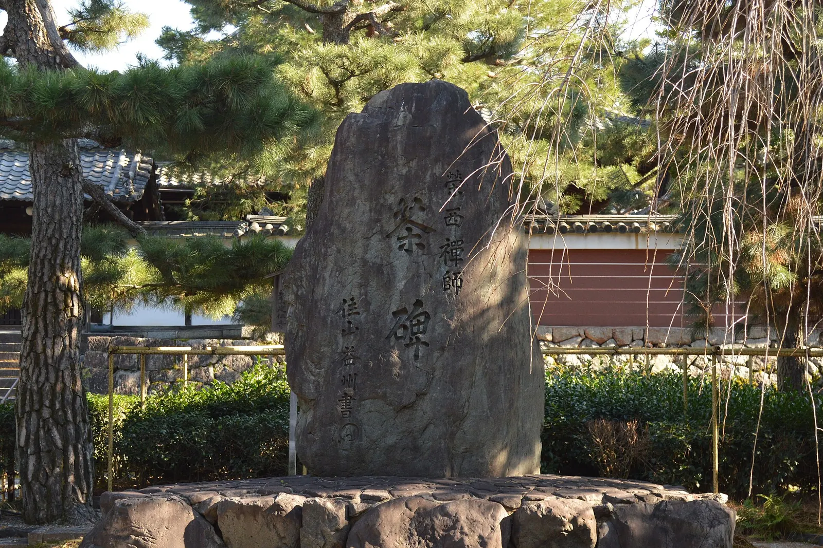 The tea monument at Kennin-ji, the Kyoto temple founded by Eisai: a tall carved stone among pine trees in front of a low red-brown wall
